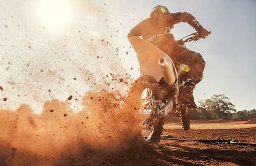 Triumph TF 250-X kicking up dirt behind bike riding away from camera