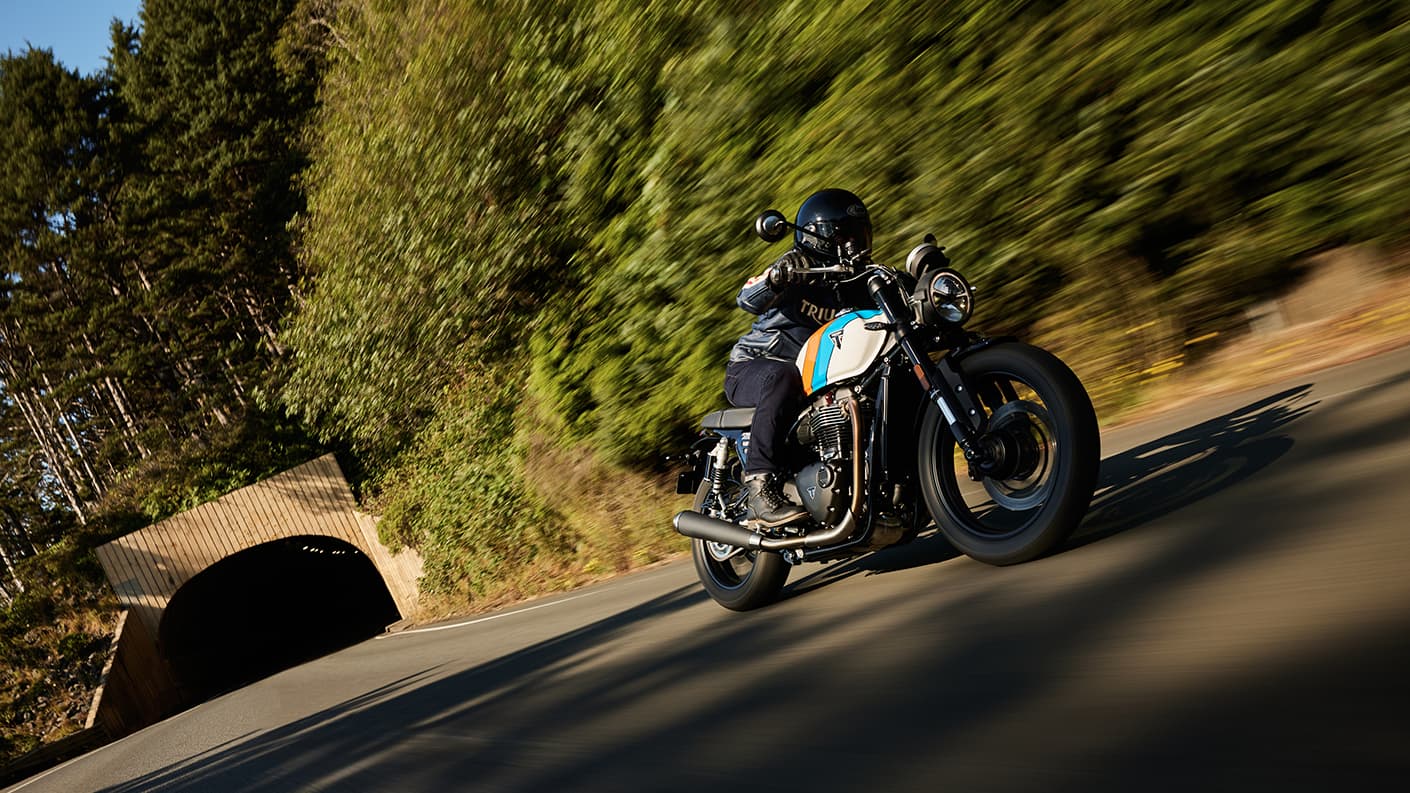 Triumph Speed Twin 900 riding towards the camera on forest lined road