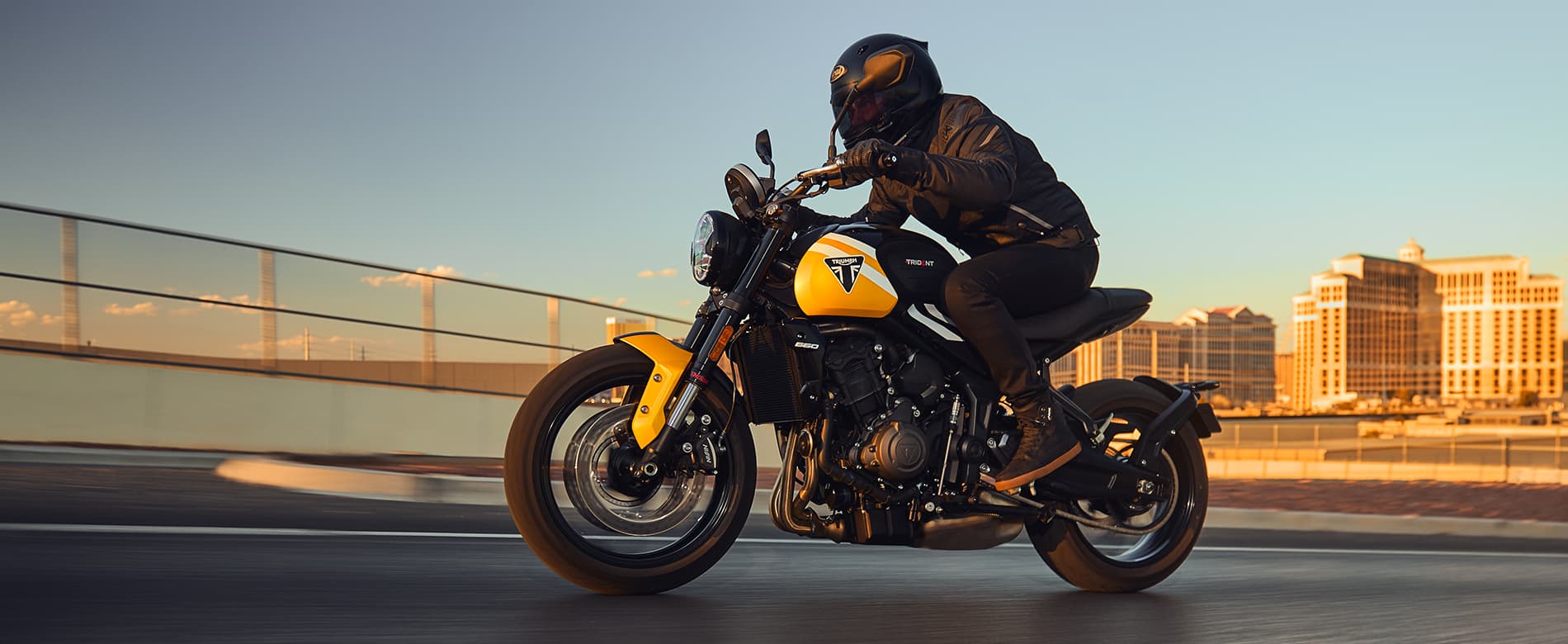 Triumph Trident 660 in cosmic yellow and sapphire black riding at sunset in urban setting