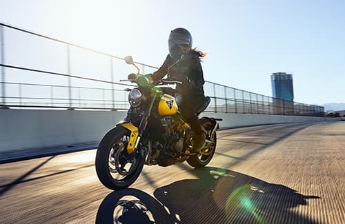 Triumph Trident 660 in cosmic yellow and sapphire riding away from urban setting