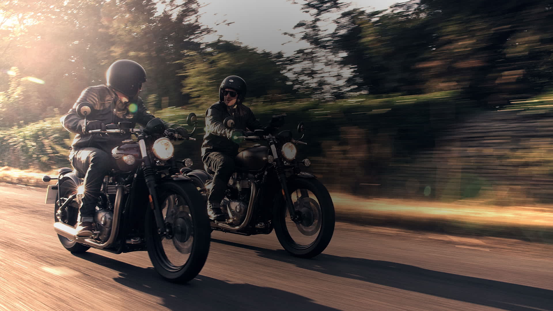 Two people riding Triumph Bobbers through a street. 